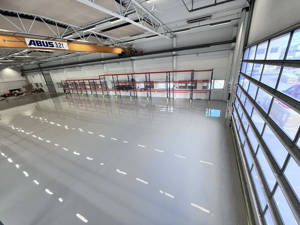 Blankt epoxygulv i lagerhall med traverskran